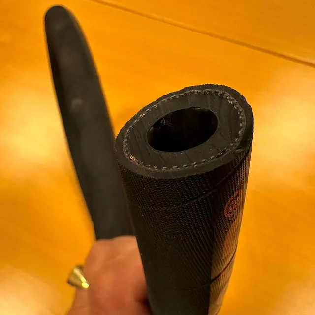 Sort, tykk gummislange holdes i hånden med tydelig sirkulært tverrsnitt.