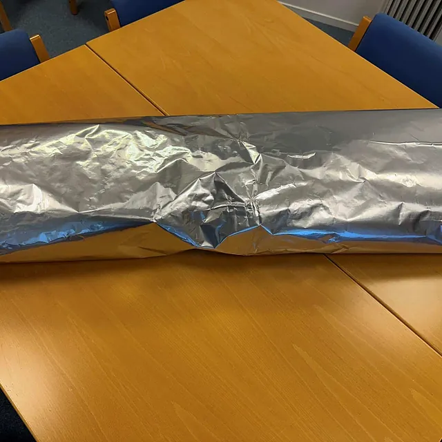 Stor rull med sølvfarget folie ligger på et møtebord med blå stoler rundt.