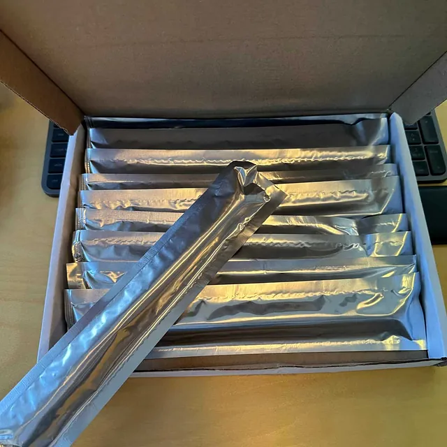 Åpen eske med flere forseglede sølvfargede patroner av VPI 580 plassert på rekke.