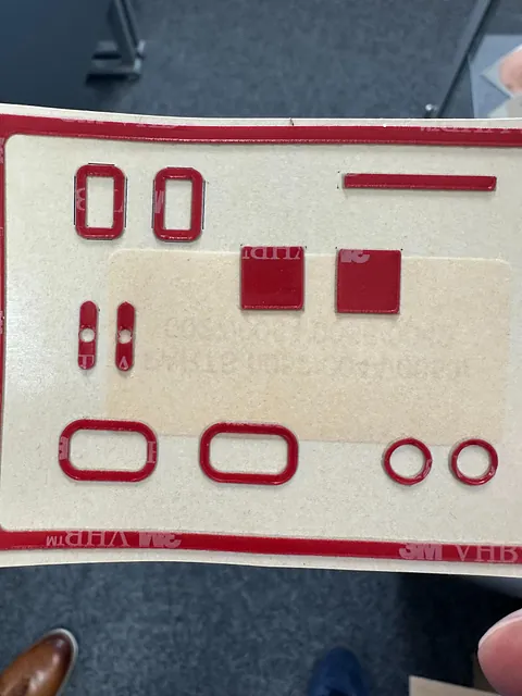 Rød dobbeltsidig 3M-tape stanset i ulike former på beige bakpapir.