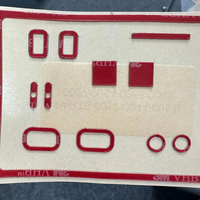 Rød dobbeltsidig 3M-tape stanset i ulike former på beige bakpapir.