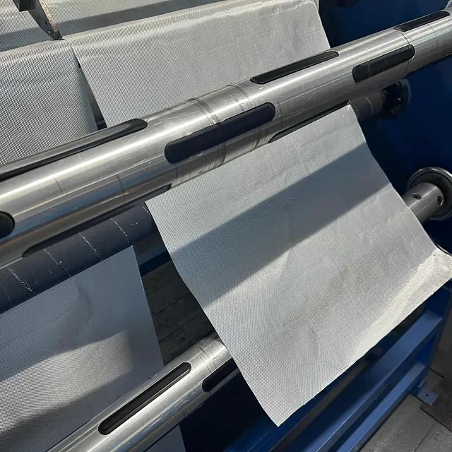 Hvit tekstilrull mates gjennom en maskin med metallruller i produksjonsmiljø.