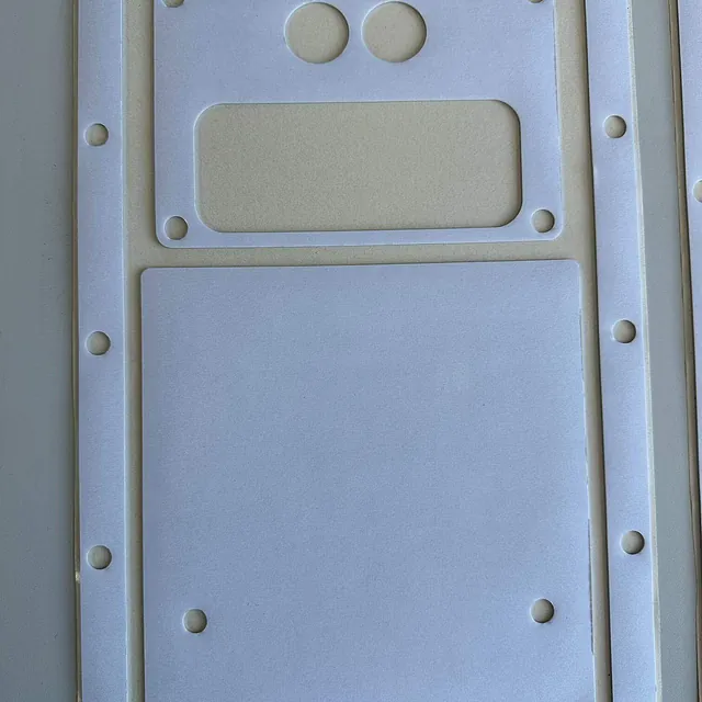 Hvit pakning med flere hull og utskjæringer ligger på et bord, klar til bruk.