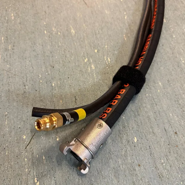 To trykkslanger med koblinger i messing og metall, festet med borrelås mot gulvet.