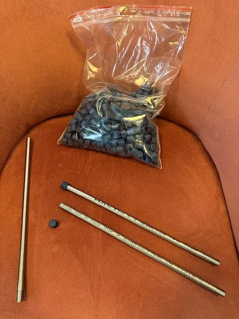 Plastpose med sorte endekapsler og tre stålrør med tekst, liggende på en oransje stol.