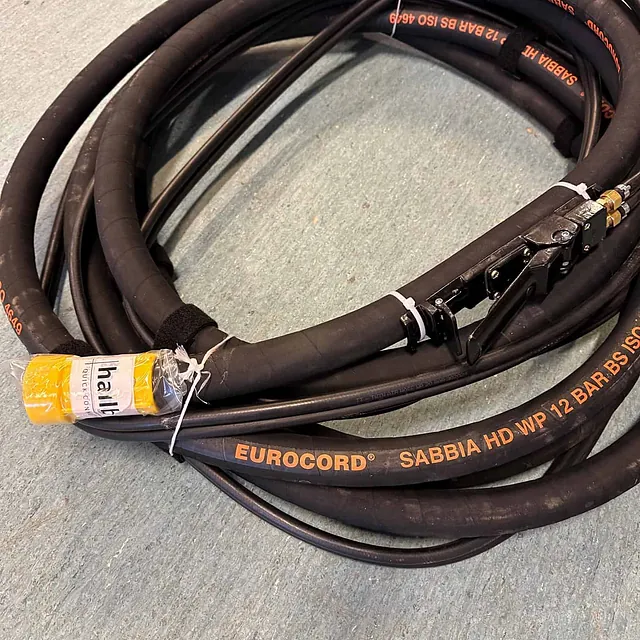 Sammenrullet slange merket “EUROCORD SABBIA HD WP 12 BAR” med ulike koblinger.