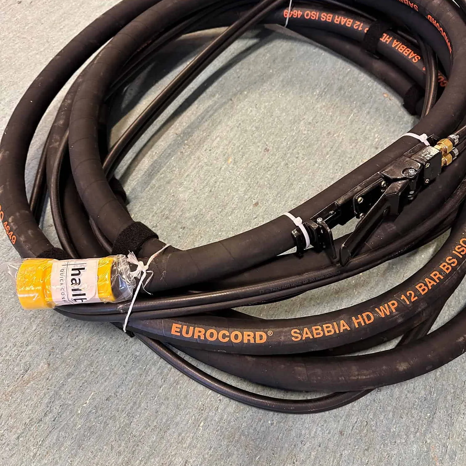 Sammenrullet slange merket “EUROCORD SABBIA HD WP 12 BAR” med ulike koblinger.
