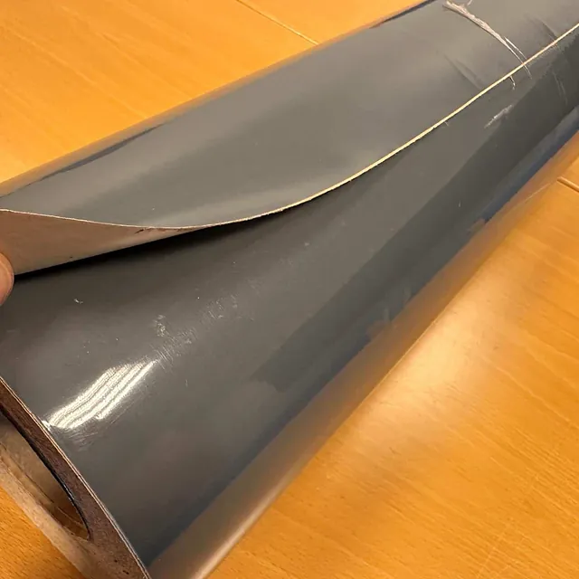 Nærbilde av rull med grå folie der en hånd løfter folien for å vise baksiden.