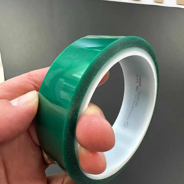 En person holder en grønn, blank rull med industriell tape mot mørk bakgrunn.