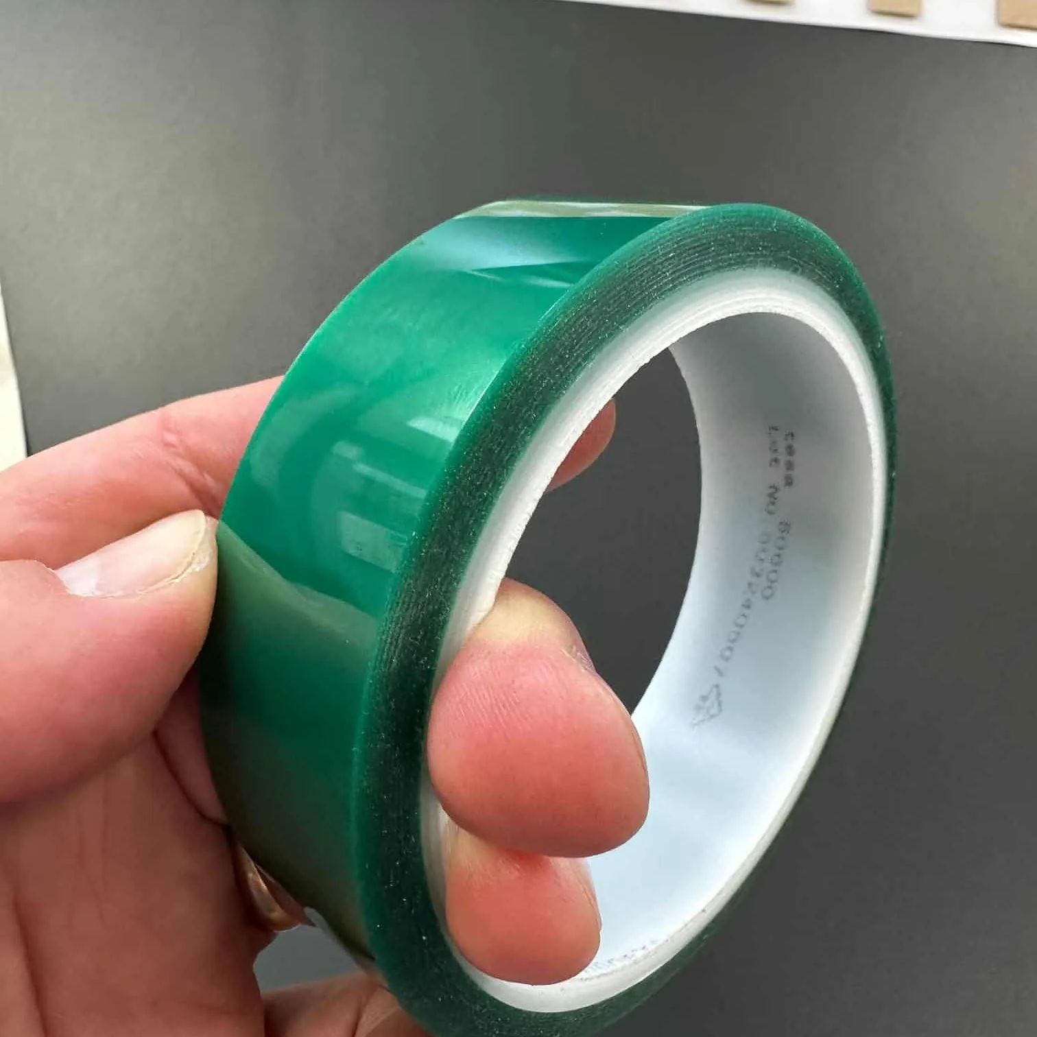 En person holder en grønn, blank rull med industriell tape mot mørk bakgrunn.