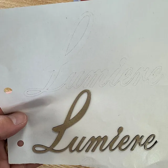 Hånd holder en papplate med utskåret ordet "Lumiere" i elegant skrifttype.