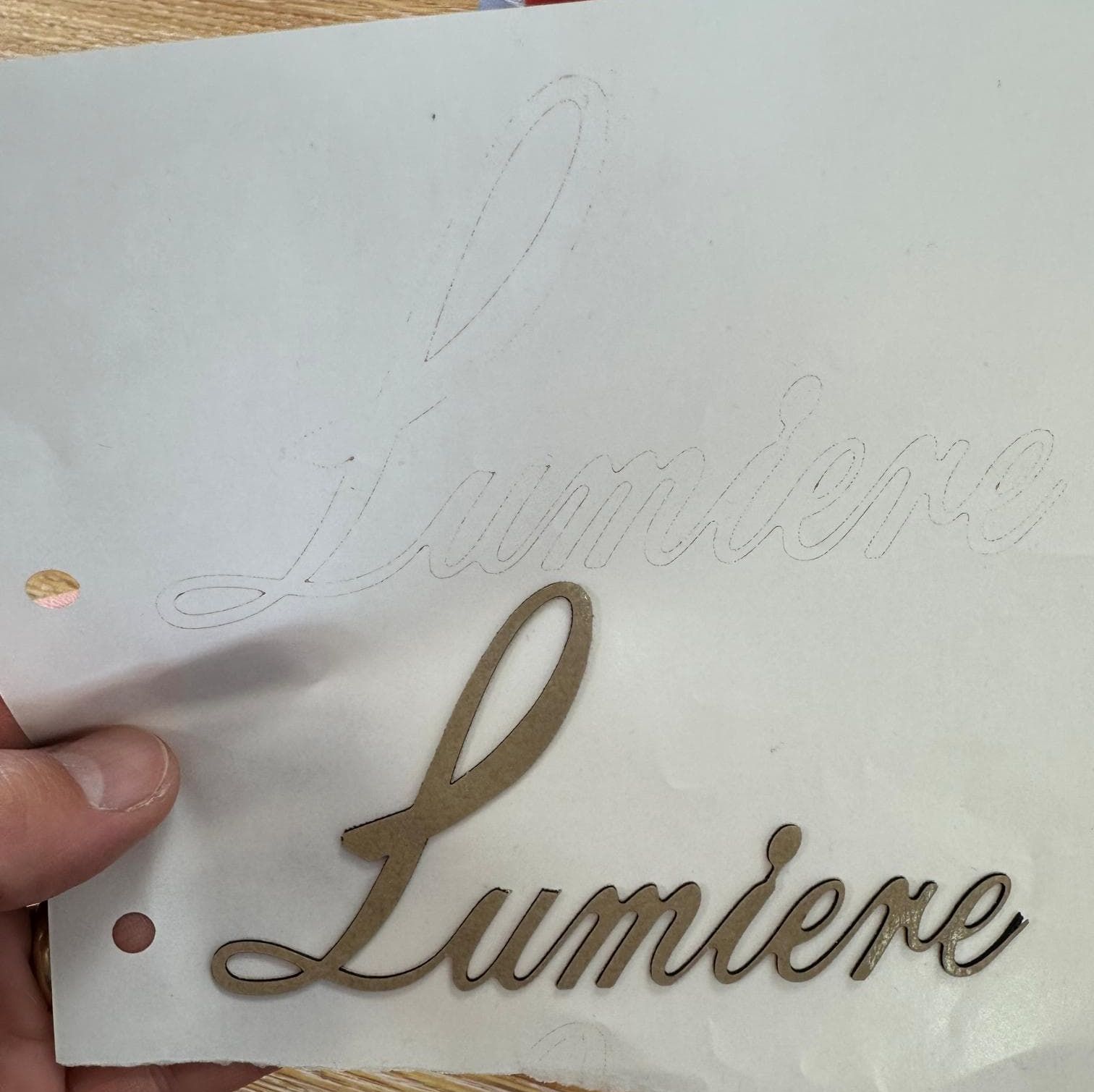 Hånd holder en papplate med utskåret ordet "Lumiere" i elegant skrifttype.