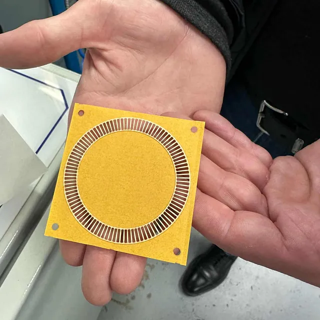 En person holder en gul firkantet del med sirkel og små åpninger i hånden.